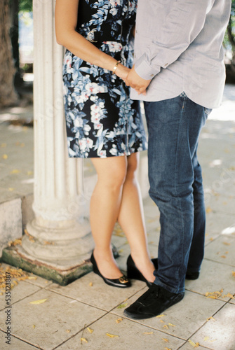 Man holds woman by the hands while standing near a column. Cropped