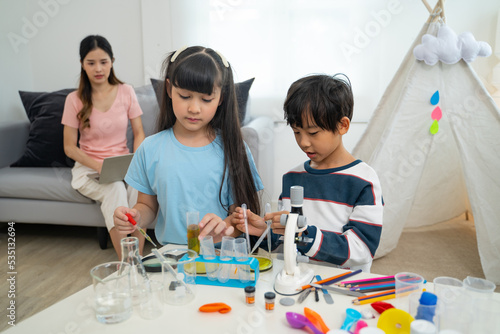 Two little scientists making chemical test with microscope in living room.