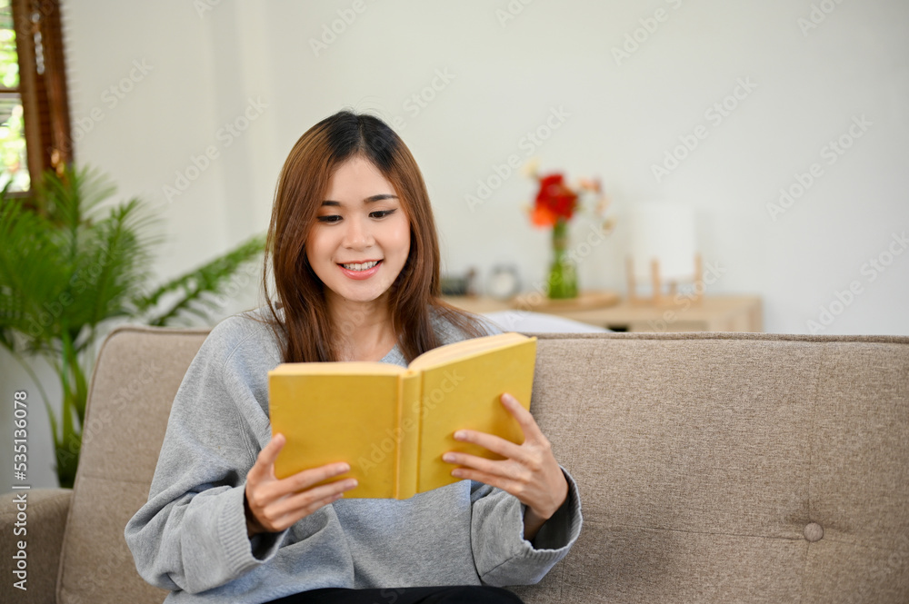 Pretty Asian female enjoys reading a book or novel while relaxing in her living room. Pretty Asian female enjoys reading a book or novel while relaxing in her living room.