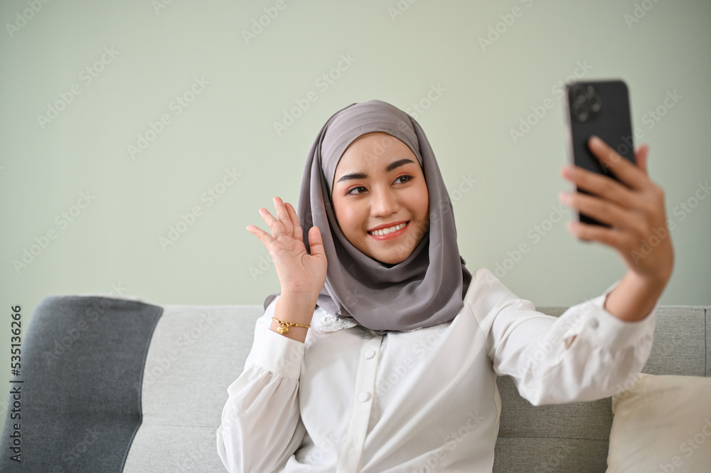 Beautiful Asian Muslim woman wearing hijab video calls her friends on her smartphone Beautiful Asian Muslim woman wearing hijab video calls her friends on her smartphone