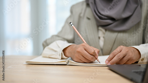 cropped, Bright Asian Muslim female college student writing something on her notebook. photo