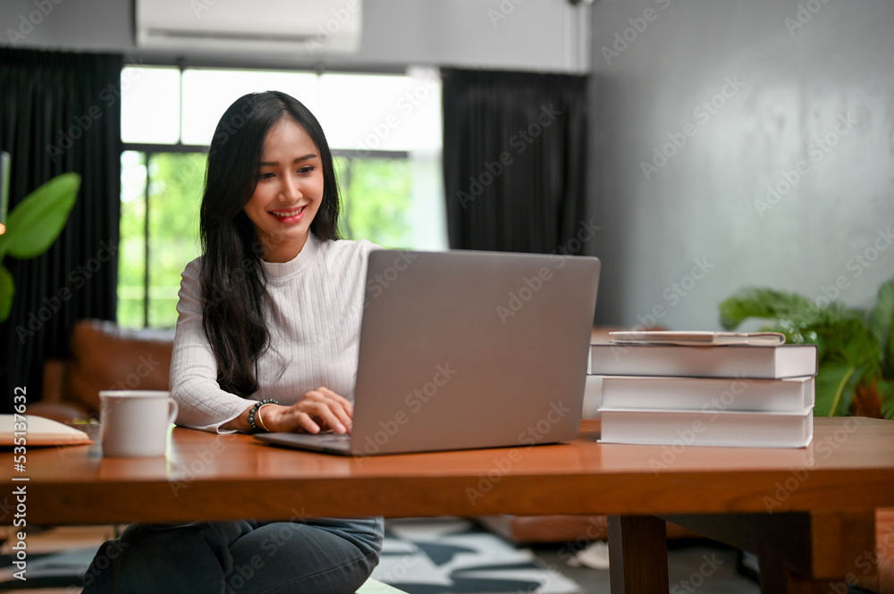 Beautiful Asian female working, browsing website, using laptop computer in her living room. Beautiful Asian female working, browsing website, using laptop computer in her living room.