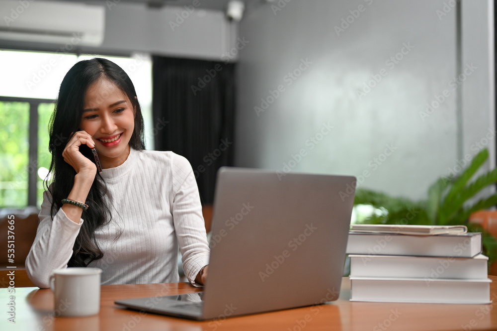 Happy Asian female freelancer in her home office, on the phone with her client Happy Asian female freelancer in her home office, on the phone with her client