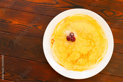 Traditional slavic pancakes or crepes on white plate, decorated with cherry and sugar. On wooden table top. Flat lay. 