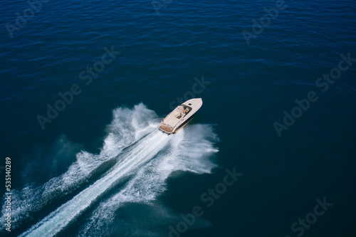 Big expensive open boat with a man moving fast on dark blue water top view. Large speed boat moving at high speed. Expensive boat fast movement on dark water top view.