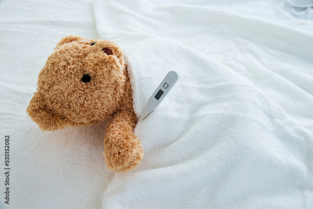 Teddy bear in bed with thermometer and bandage