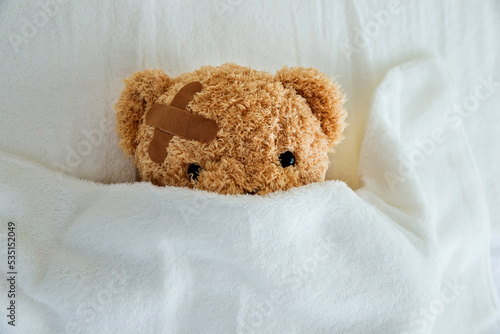 Teddy bear with bandaged head ill in bed