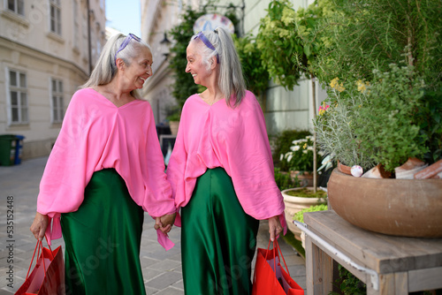 Senior women twins in colourful clothes in city, shopping.