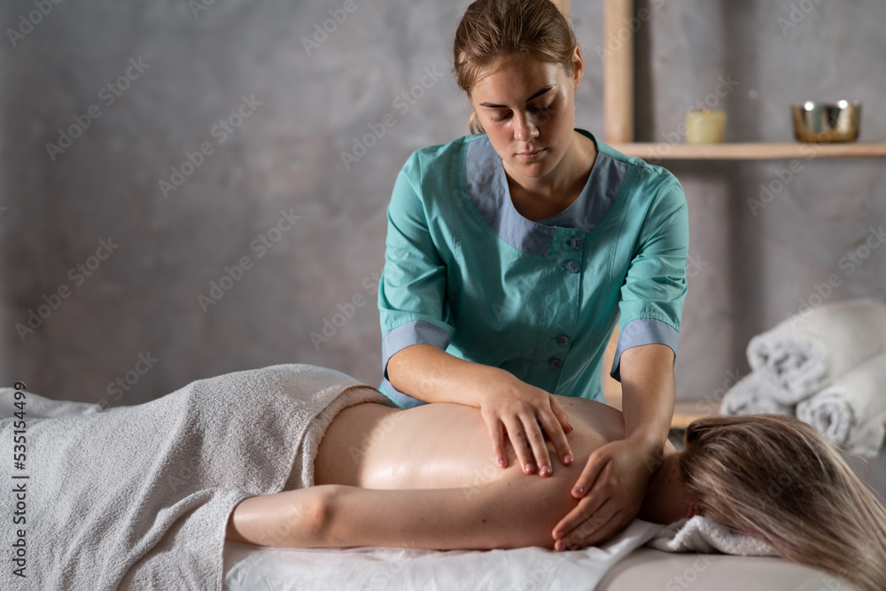 Masseuse massaging back and shoulder blades of young woman lying on massage table in the spa salon. Massage spa treatments. Masseuse massaging back and shoulder blades of young woman lying on massage table in the spa salon. Massage spa treatments.