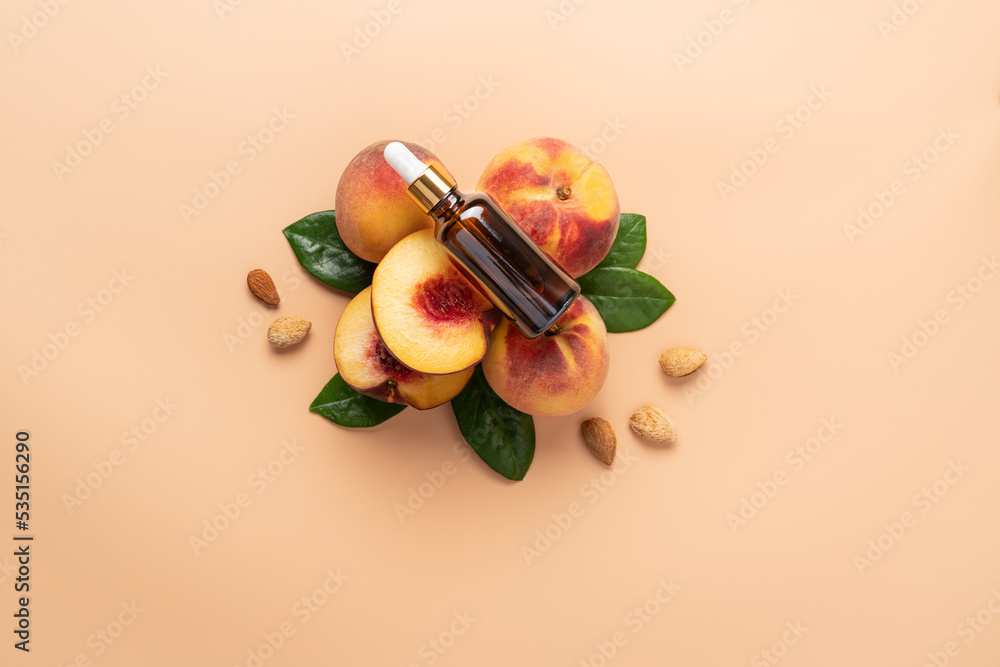 Serum or oil in glass bottle lying on composition of neatly arranged ripe peaches, green leaves and almond pits on beige background. Beauty or medicine concept Serum or oil in glass bottle lying on composition of neatly arranged ripe peaches, green leaves and almond pits on beige background. Beauty or medicine concept