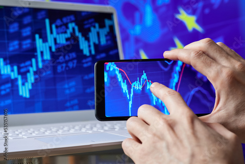 Trader analyzes stock market data in smartphone on the background of stock charts