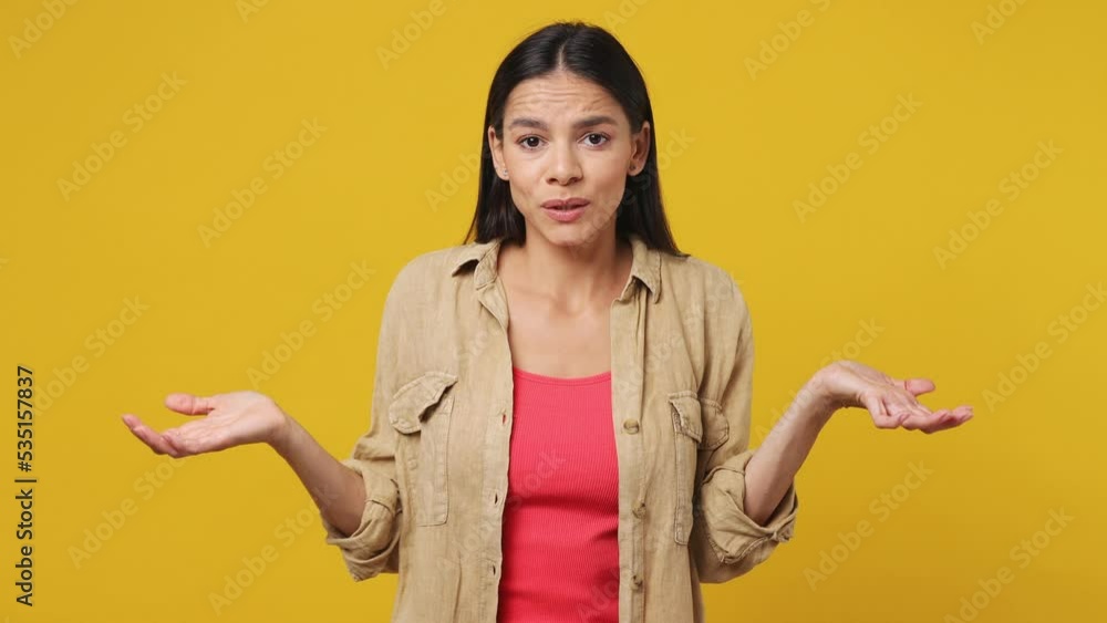 Young fun confused shy shamed latin woman she wear beige shirt pink t-shirt look camera spreading hands say oops ouch oh omg i am so sorry isolated on plain yellow background. People lifestyle concept Young fun confused shy shamed latin woman she wear beige shirt pink t-shirt look camera spreading hands say oops ouch oh omg i am so sorry isolated on plain yellow background. People lifestyle concept