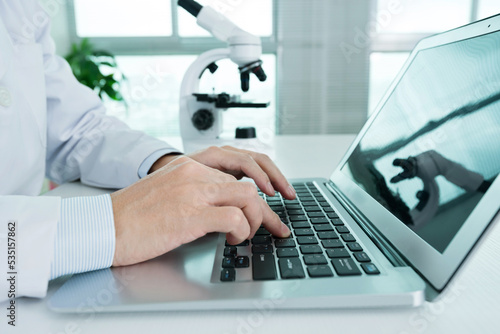 Scientist using laptop computer and microscope