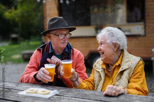Happy senior couple in forest buffet resting after walk, having beer and small cake.