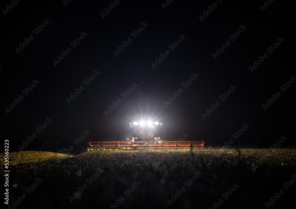 Front view of combine harvester working in a field at night during the last days of harvesting season
