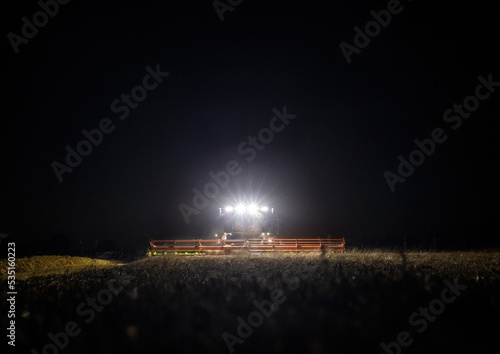 Obraz na płótnie Front view of combine harvester working in a field at night during the last days of harvesting season w salonie