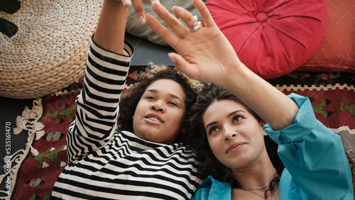 Close-up portrait of beautiful ethnically diverse lesbian couple relaxing on floor close to each other touching fingers