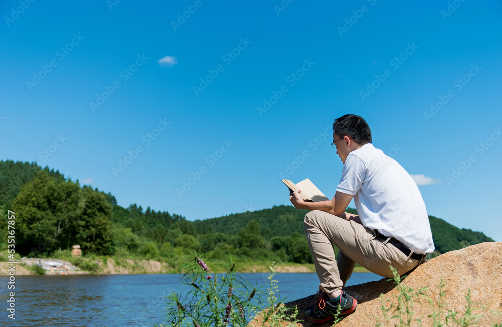 Young man enjoying reading a book by the lake