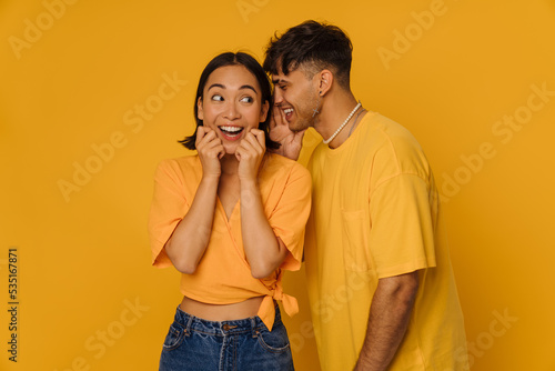 Young stylish smiling man whispering to beautiful enthusiastic asian woman