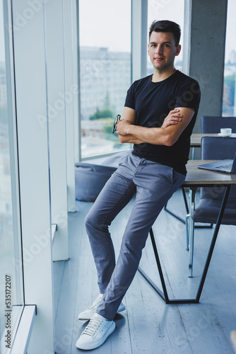 Obraz na plátně Portrait of a smiling young man in a black t-shirt against the background of a modern office