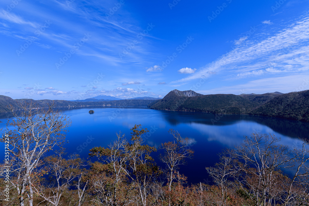 青空を湖面に映す湖と初秋の木々。日本の北海道の摩周湖。