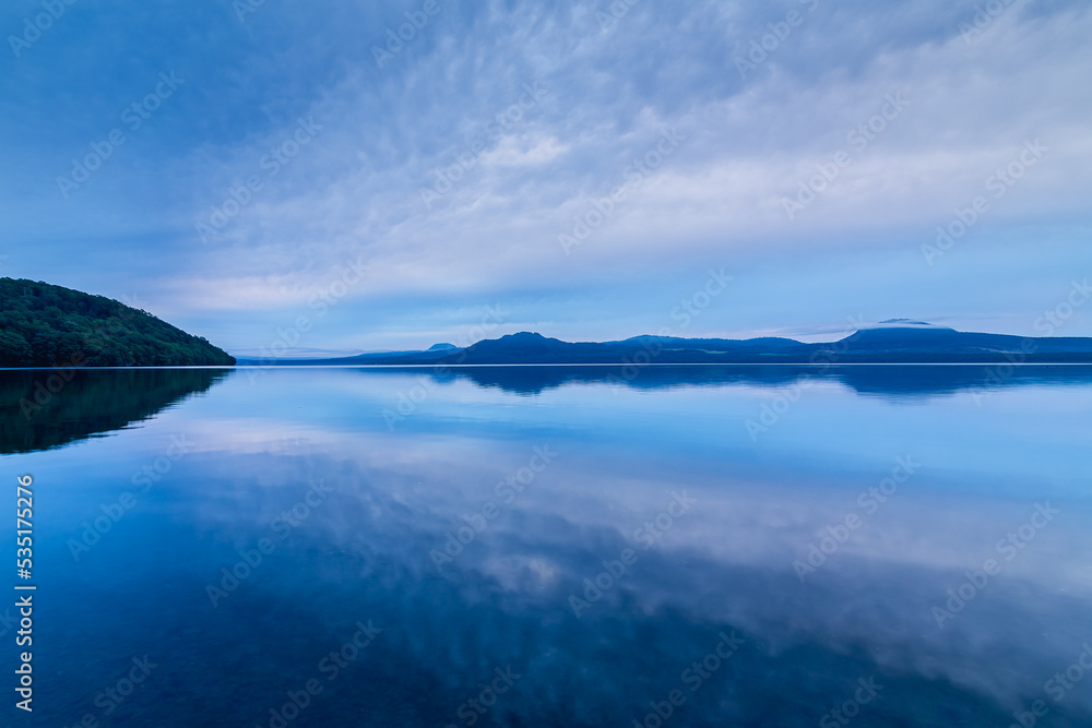 曇り空を湖面に反射する夜明けの湖。北海道の屈斜路湖。