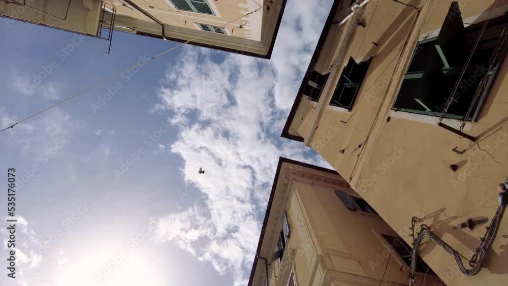 SLOWMOTION: Low-Angle view of old italian houses in Imperia. Bird crossing the blue sky from right to left. SLOWMOTION: Low-Angle view of old italian houses in Imperia. Bird crossing the blue sky from right to left.