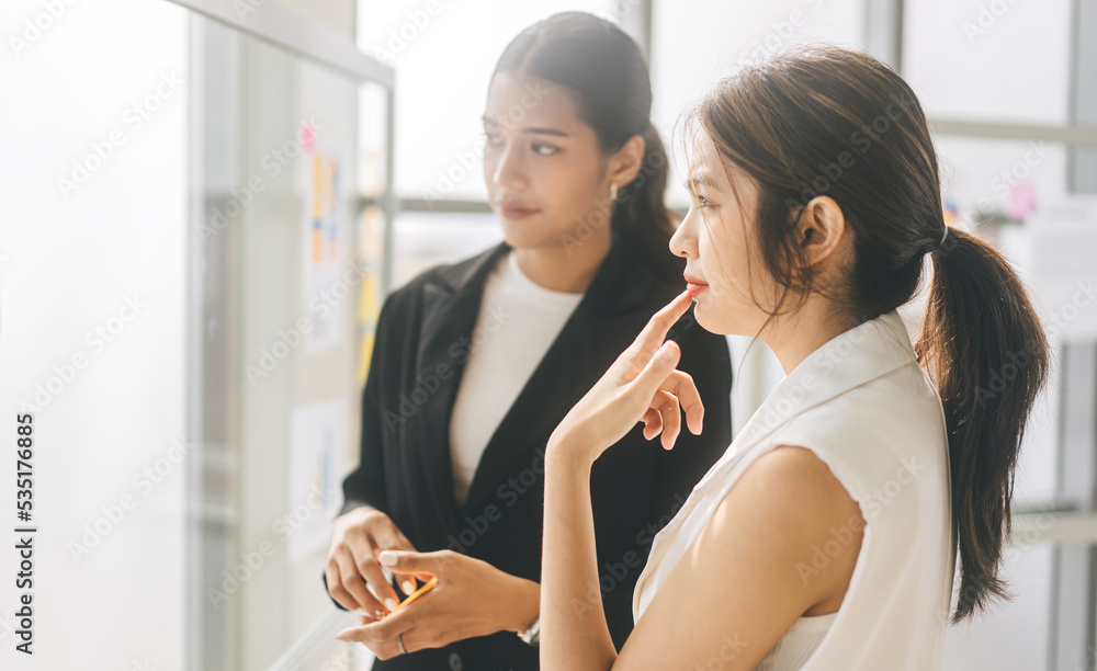 Two young adult asian woman wearing suit talking about strategy in office Two young adult asian woman wearing suit talking about strategy in office