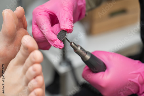 Woman on professional pedicure procedure by abrasive disc machine in beauty salon. 