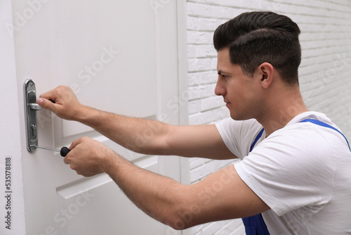 Handyman with screwdriver repairing door lock indoors