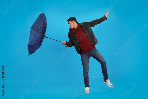 Fotografia Man with umbrella caught in gust of wind on light blue background