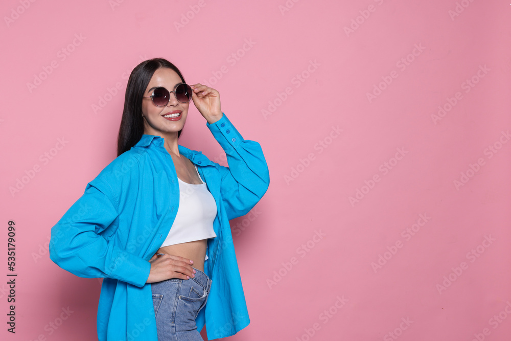 Attractive happy woman touching fashionable sunglasses against pink background. Space for text Attractive happy woman touching fashionable sunglasses against pink background. Space for text