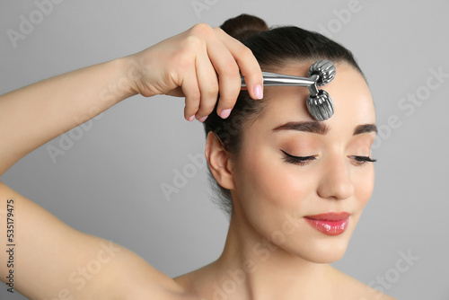Woman using metal face roller on grey background