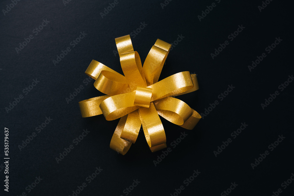 Golden bow for present on black background. Top view. Black friday or Christmas holidays concept Golden bow for present on black background. Top view. Black friday or Christmas holidays concept