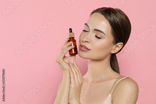 Young woman with bottle of essential oil on pink background, space for text