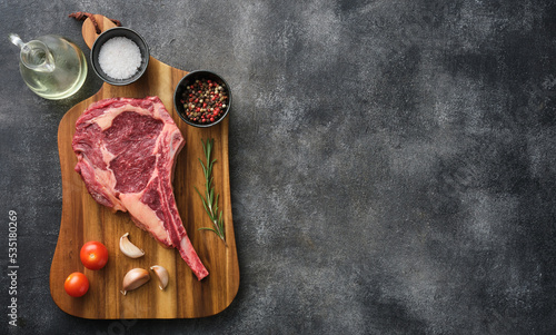 Raw Tomahawk steak on wooden board with spices for grilling, copy space for text