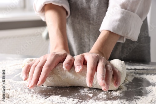 Woman kneading dough at table in kitchen, closeup