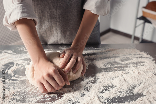 Woman kneading dough at table in kitchen, closeup