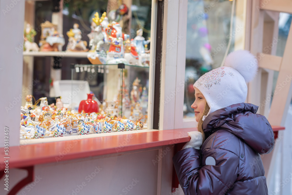 The girl looks at the window and chooses souvenirs. Christmas Fair.