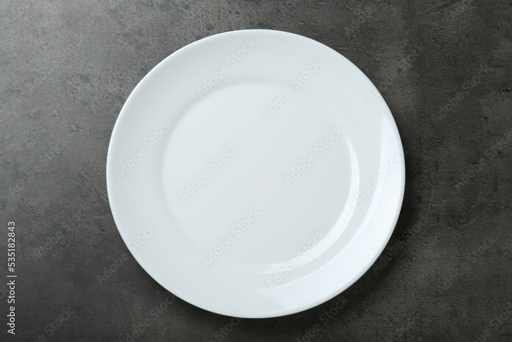 Empty white ceramic plate on grey table, top view Empty white ceramic plate on grey table, top view