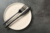 Beige ceramic plate with cutlery on grey table, top view. Space for text