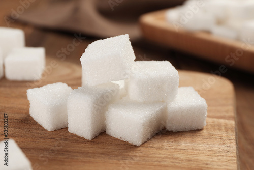 Refined sugar cubes with wooden board on table, closeup