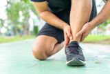 Young male in sports outfits black injured his ankle during exercise in the park. Low section of sports man suffering from flipped ankle while sitting on track during. Accident from exercise concept.
