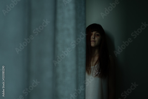 Female ghost in white dress in room. A young scary girl in an old white dress staring in to the camera ferociously with dark background. Asian woman make up ghost face at house. Scary horror concept.