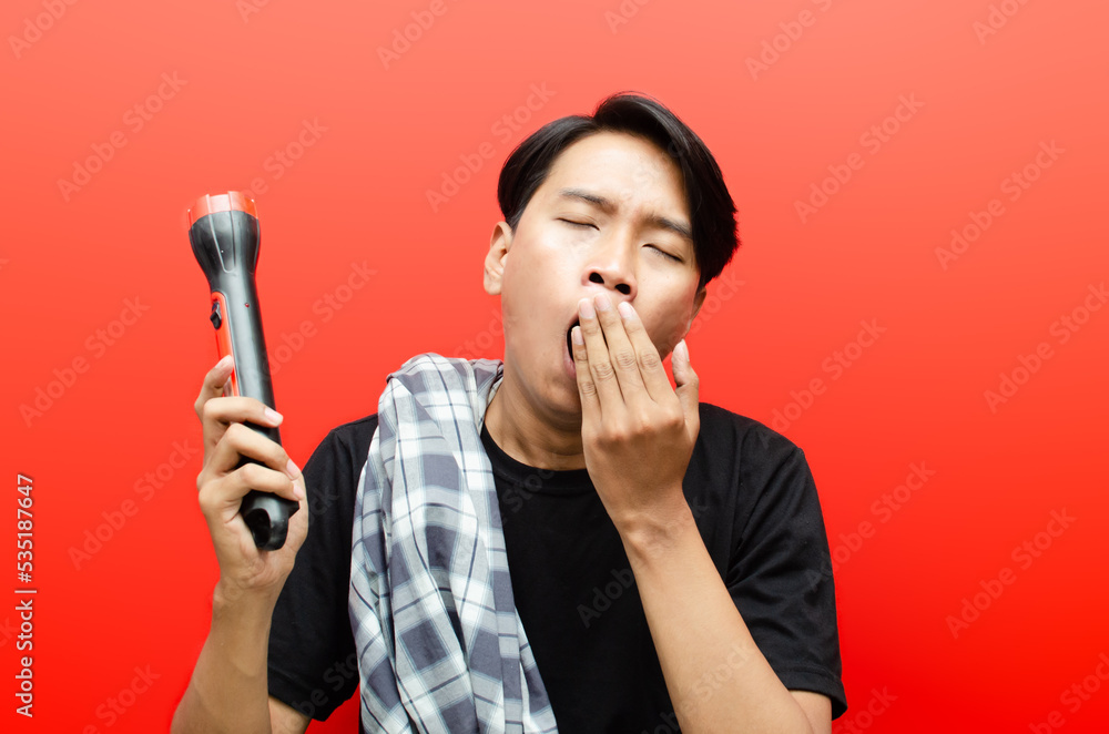 Asian man with sleepy expression covering mouth. indonesian man yawning while holding sarong and flashlight doing patrol or ronda. Asian man with sleepy expression covering mouth. indonesian man yawning while holding sarong and flashlight doing patrol or ronda.