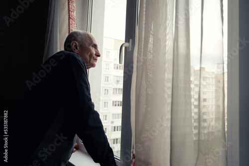 Quadro em tela Grandfather looking through window glass covered with transparent white curtain