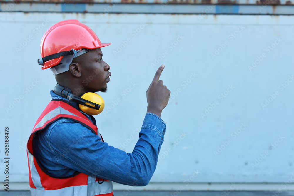 Foreman engineer standing and crossed arms while pointing something with happy and success face. Confident engineering work at container cargo site and checking industrial container cargo freight ship