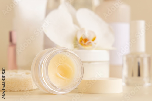 Smass Glass jar and other cosmetics near white orchid flower on beige close up