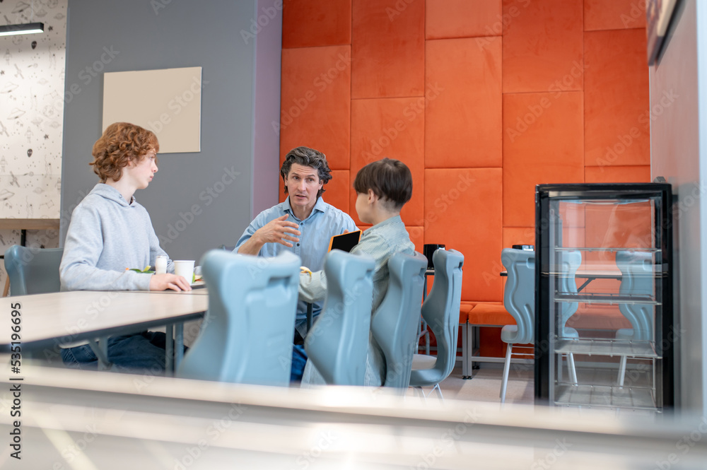 Schoolteacher having a conversation with his pupils at lunch Schoolteacher having a conversation with his pupils at lunch