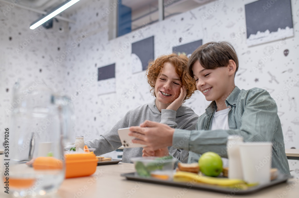 Two cheerful schoolmates sitting in the school canteen